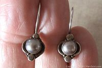Close-up photo of front view of two sterling silver earrings with bezel set round grey pearls being held in fingers.