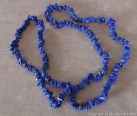 Full view of the long blue Lapis Lazuli chip gemstone necklace laid out on a surface.