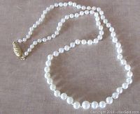 Full view of the pearl necklace laid out flat on a surface, showing the full length, pearls, and clasp.