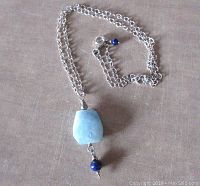 Full view of the necklace showing the chain, aquamarine pendant, small lapis beads, and lobster clasp.