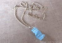 Photo of light blue wired fibre optic glass cat pendant on silver chain laid on neutral surface.