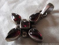 Close-up of front of pendant showing deep red garnet gemstones arranged in a cross shape with polished silver setting.