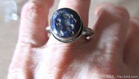 Top view of the ring worn on a finger showing the pitted lapis lazuli stone round shape and setting.