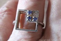 Front view of the square open work ring showing the textured silver with four small blue stones in one corner.