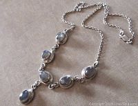 Top view of the sterling silver labradorite necklace laid flat on a beige fabric surface showing the linked chain, lobster clasp, and six oval labradorite stones in bezel settings.