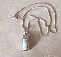Pendant with light blue-green rectangular larimar gemstone set in polished sterling silver, shown laying flat on surface with chain loosely coiled.