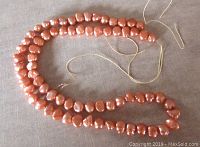Photo of an orange freshwater pearl strand, showing irregularly shaped pearls on a string without clasp.