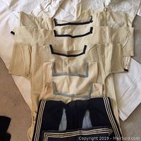 Four white cotton sailor tops laid out, showing various navy and light blue neck stripes