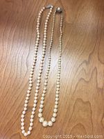 Two vintage faux pearl necklaces displayed on a wooden surface.