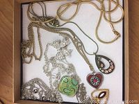 Full view of seven necklaces laid out in jewelry box showing variety of pendants and chains.