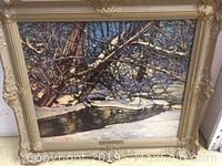 Front view of the framed print showing a winter landscape with snow and a reflective stream in a decorative gold wood frame approximately 24.5 by 28 inches.