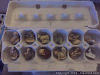 Top-down view of a recycled egg carton holding 12 small ceramic figurines depicting various animals and objects.
