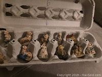 Top view of figurines placed in an egg carton, showing multiple ceramic tea figurines arranged neatly.