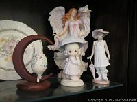 Overview of all figurines displayed together on shelf including plate behind and crescent flower vase