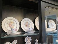 Shelved display of Edwin M. Knowles plates with floral patterned tea cups and saucers.