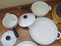 white enameled saucepans and sauté pan with lids and yellow cast iron dish