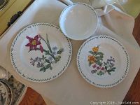 Close-up of one dinner plate, one salad plate, and one bowl, all with floral designs and green leaf vine border