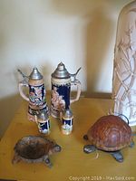 Photo shows a large blue German musical stein with metal lid, two matching smaller salt and pepper steins with metal tops, and two turtle-themed items: a turtle-shaped light and a turtle ashtray with detailed designs.