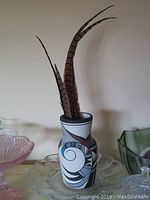 Full view of 9 inch Hopi pottery vase with feathers inside on a clear glass plate, showing the geometric spiral painted designs in black, white, blue, and brown.