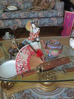 Overview of the tea pot, fan, figurine, and knife grill fork combo on a glass table showing details and arrangement