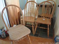 Four wooden side chairs with spindle backs and turned legs, one with a woven cushion on the seat.