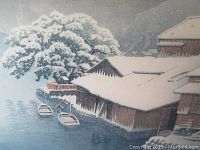 Close view of framed print showing lakeside huts and two boats under snow.