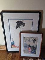 Overview of both framed prints leaning against wall on hardwood floor