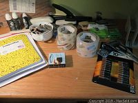 Photo showing various office items laid on desk including staplers, adhesive tapes, batteries, pens, thumbtacks, and a yellow notebook.