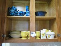 Cupboard shelf with blue Narco dishes and vases on top shelf, yellow mugs and sunflower ceramic pieces on bottom shelf, some chips noted on Narco dishes.