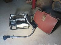 Photo of the vintage black Dictaphone with flexible microphone arm alongside the brown carrying case with metal latch.