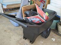 Black plastic wheelbarrow with contents inside including box and tools