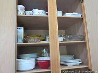 Wooden cabinet storage showing various bowls, plates, and glass dishes on shelves