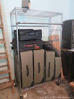 Front view of metal rolling wire shelf filled with multiple carrying cases in black and olive green.