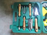 Green plastic case containing four garden hand tools with wooden handles: trowel, cultivator, transplanter, and weeder.