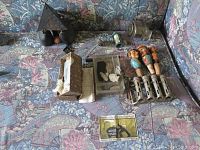 Full lot composition showing various items on a floral couch including metal coin changer, pencil sharpener, thermostat, carved bottle stoppers, and miscellaneous items.