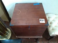 Top view of the wooden filing cabinet showing brown wood surface with minor scratches, metal corner protectors, and lock with key