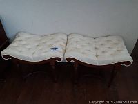 Two vintage wooden benches side by side, showing off-white tufted cushions with light yellow buttons, one button missing, placed on dark wooden floor.
