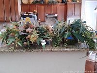 Wide shot of the two glass bowls filled with artificial greenery on a kitchen counter.