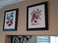 Two black-framed botanical drawings featuring cherries and peach on a beige wall.
