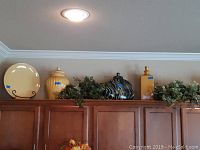 Yellow ceramic 17-inch round plate on black metal stand, yellow ceramic containers, and greenery above kitchen cabinets.