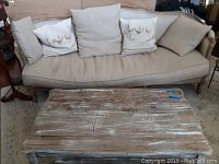 Neutral beige fabric couch with three cushions and antler motif decorative pillows, positioned against a wall.