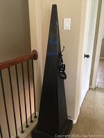 Single tall black decorative obelisk standing near stair railing, showing hanging hooks and cords.