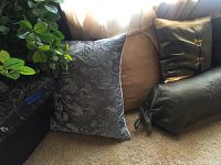 Two dark blue pillows, one with floral damask pattern, one medium brown pillow, and one square gold pillow partially visible