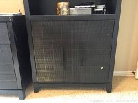 Closed view of dark wood bookcase with two doors and visible contents on top of bookcase.