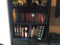 Bookshelf containing a variety of classic hardback books with gold and colored spines, neatly arranged in two rows on two shelves.