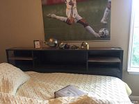 Wide shot of metal and wood sideboard placed against wall, with several metal decorative pieces and clocks on top, next to a twin bed with bedding.