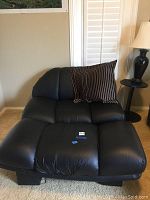 Black tufted leather double chair with wide seating and a brown striped pillow placed on it.