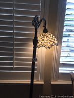 Full view of Tiffany style floor lamp with stained glass shade lit, showing ornate metal base and stand.
