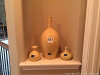 Set of three yellow ceramic vases on white shelf, largest in center, two smaller on either side.