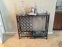Full view of marble and iron bar cart with glass shelves and bottle rack, glasses and decanters on top and shelves